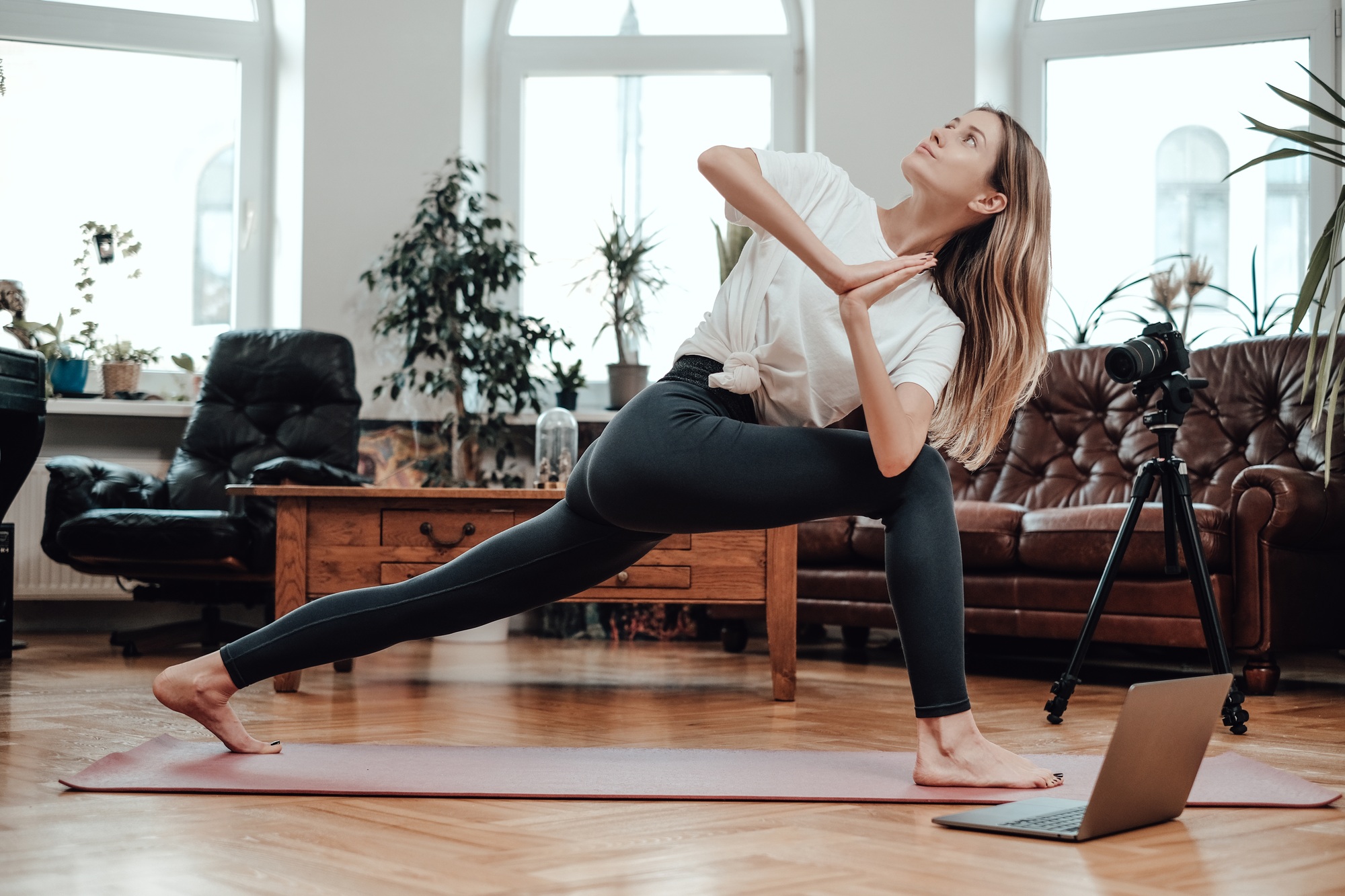 Female athlete does yoga with laptop and photocamera in room