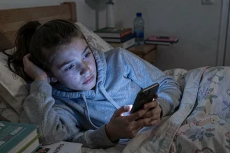 Adolescente française fatiguée qui consulte son smartphone la nuit dans sa chambre, illustrant l'impact des réseaux sociaux sur le sommeil des jeunes